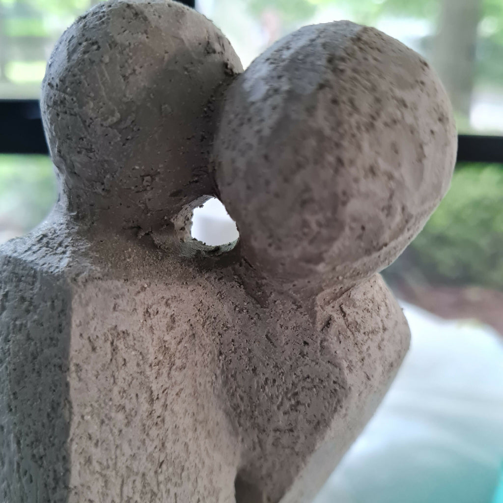 Sculpture en argile claire : gros plan sur deux corps enlacés, texture granuleuse