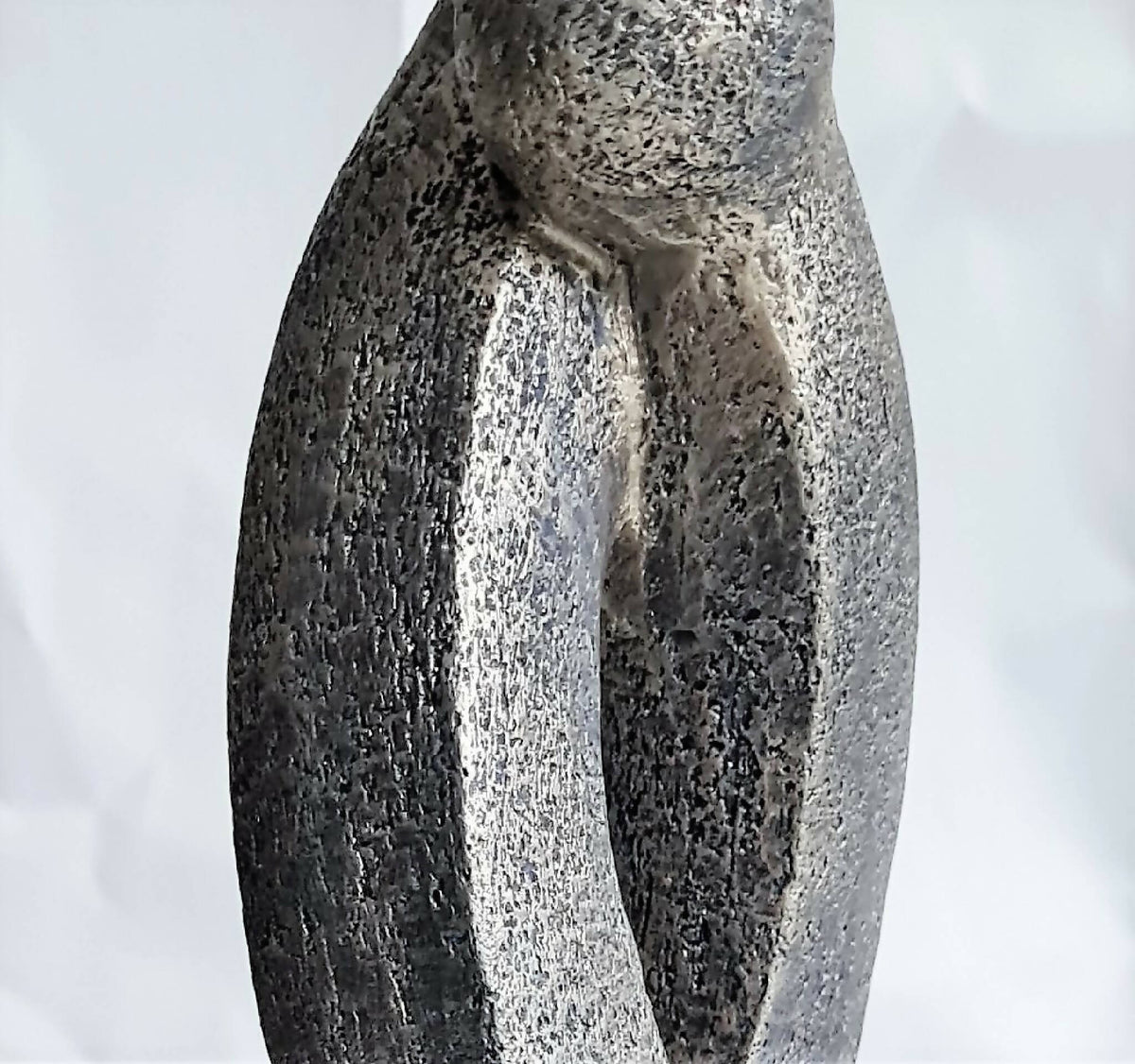 Sculpture en argile grise texturée, deux formes entrelacées avec ouverture en U.