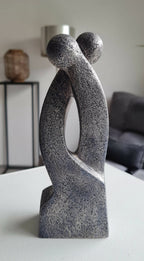 Sculpture en argile grise, silhouette en double courbe avec ouverture ovale et base droite.