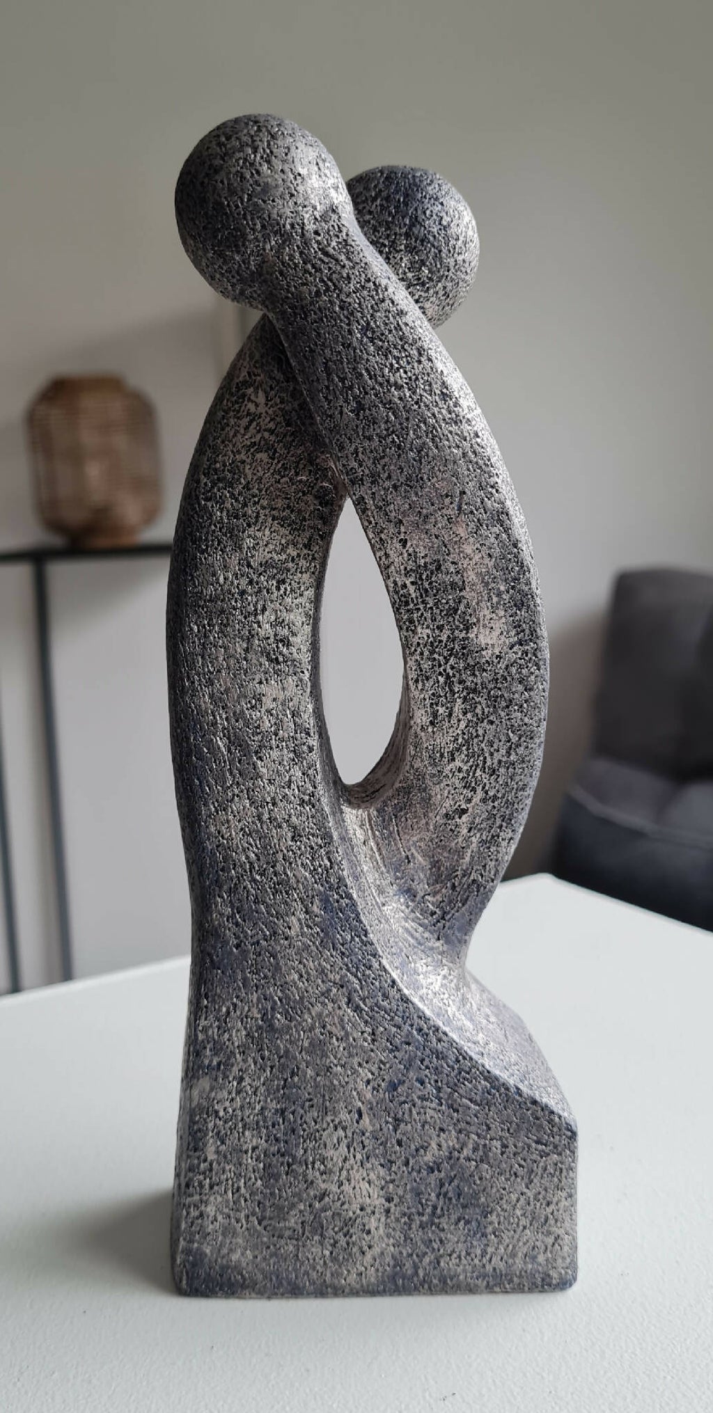 Sculpture en argile grise texturée, forme double en S avec ouverture centrale et base.