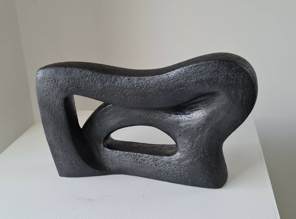 Sculpture abstraite sombre aux courbes sinueuses, trois ouvertures ovales visibles.