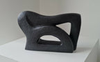 Sculpture abstraite sombre, vue de profil, grandes ouvertures en forme de triangle.