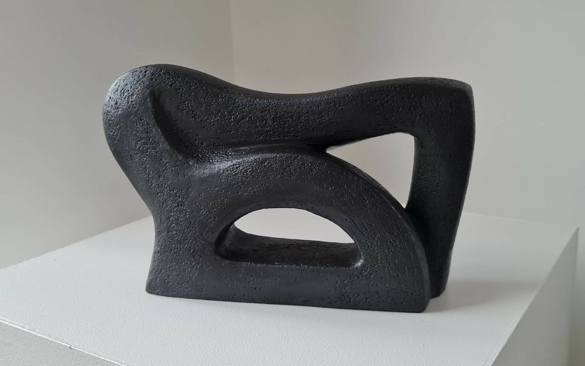 Sculpture abstraite sombre, vue de profil, grandes ouvertures en forme de triangle.