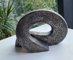 Sculpture abstraite en pierre sombre, boucle ovale posée sur une surface