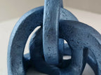 Sculpture abstraite bleue, vue rapprochée des anneaux ajourés et tige verticale.
