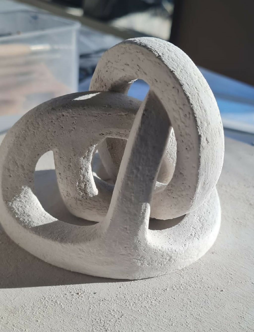 Sculpture abstraite en résine gris clair, anneaux ajourés et tige verticale sur base.