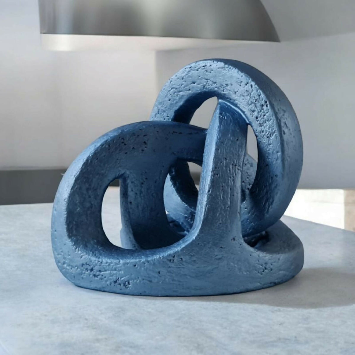 Sculpture abstraite en résine bleue, anneaux entrelacés sur socle rectangulaire.
