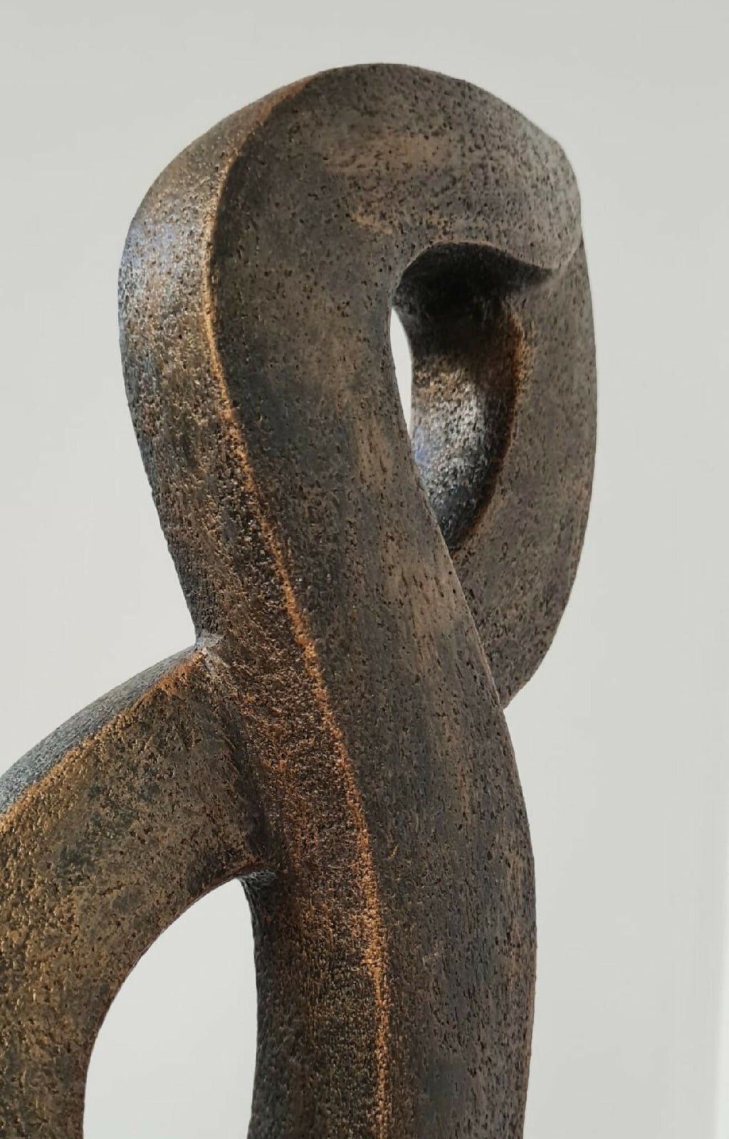 Sculpture en argile texturée brun, vue rapprochée de la boucle ajourée.