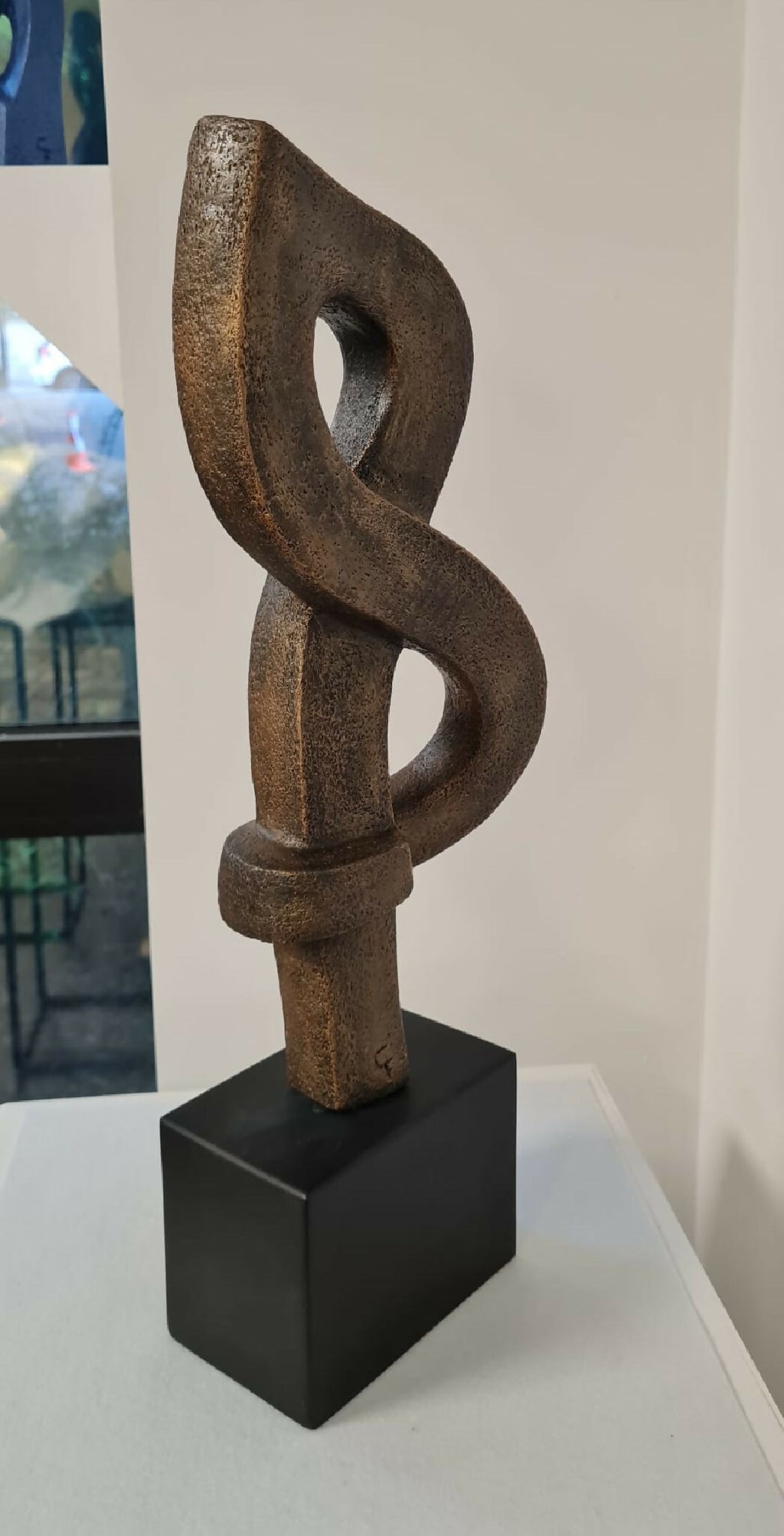Sculpture abstraite en argile brun foncé, entrelacement sur socle noir cubique.