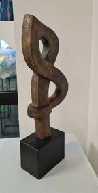 Sculpture abstraite en argile brun foncé, entrelacement sur socle noir cubique.