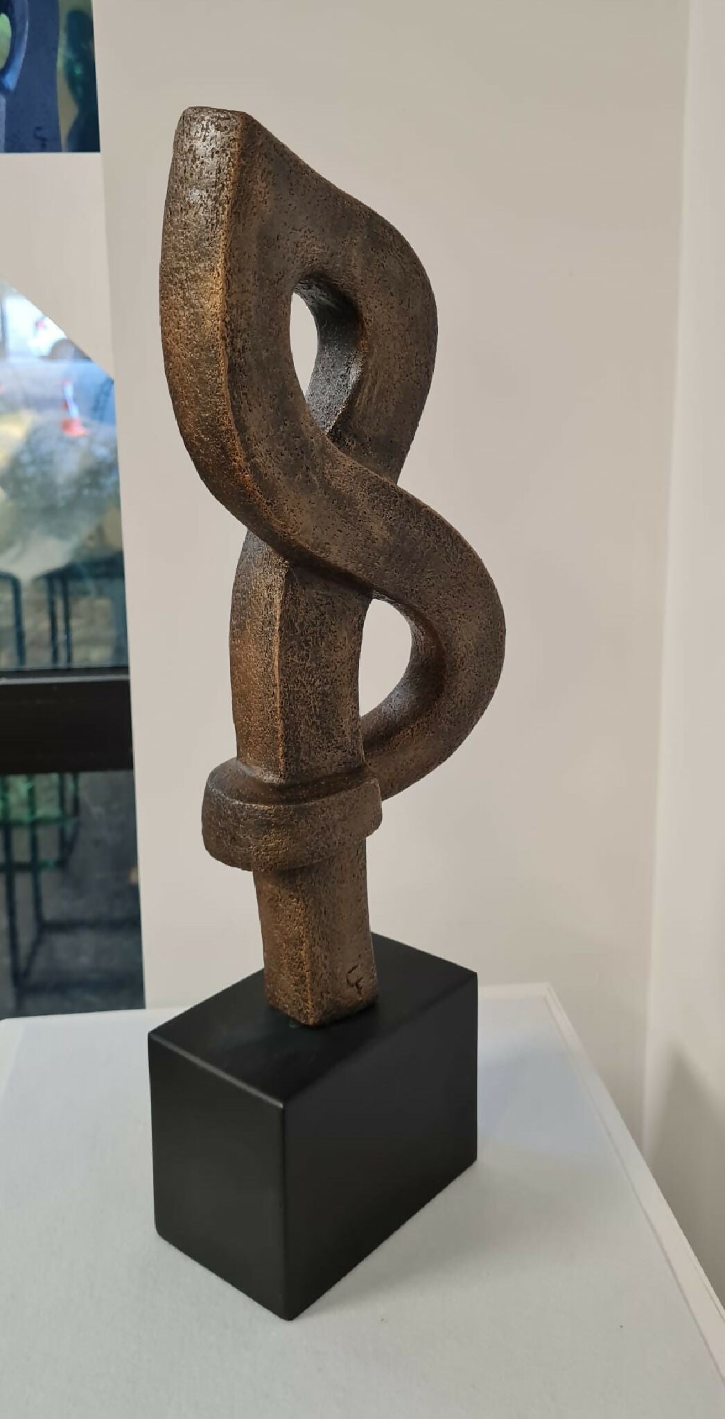 Sculpture abstraite en argile brun foncé, entrelacement sur socle noir cubique.
