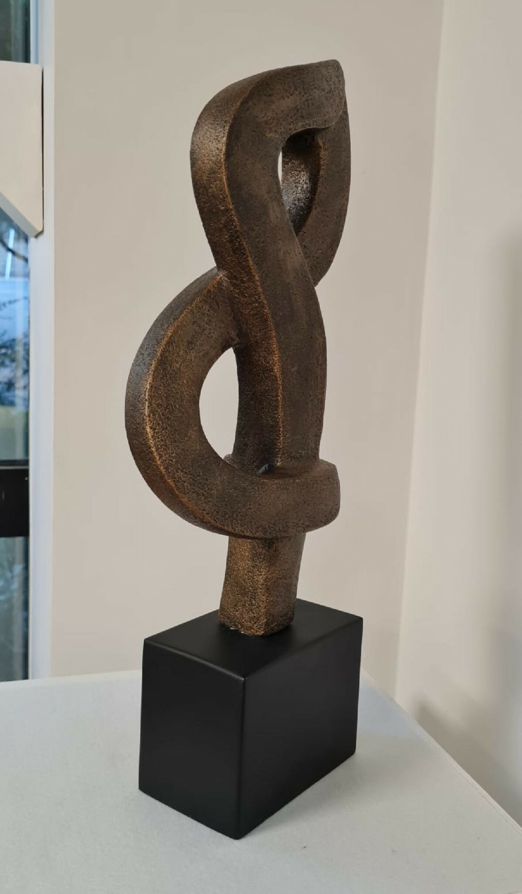 Sculpture contemporaine en argile brun, forme en anneaux sur socle noir.