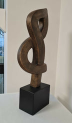 Sculpture contemporaine en argile brun, forme en anneaux sur socle noir.