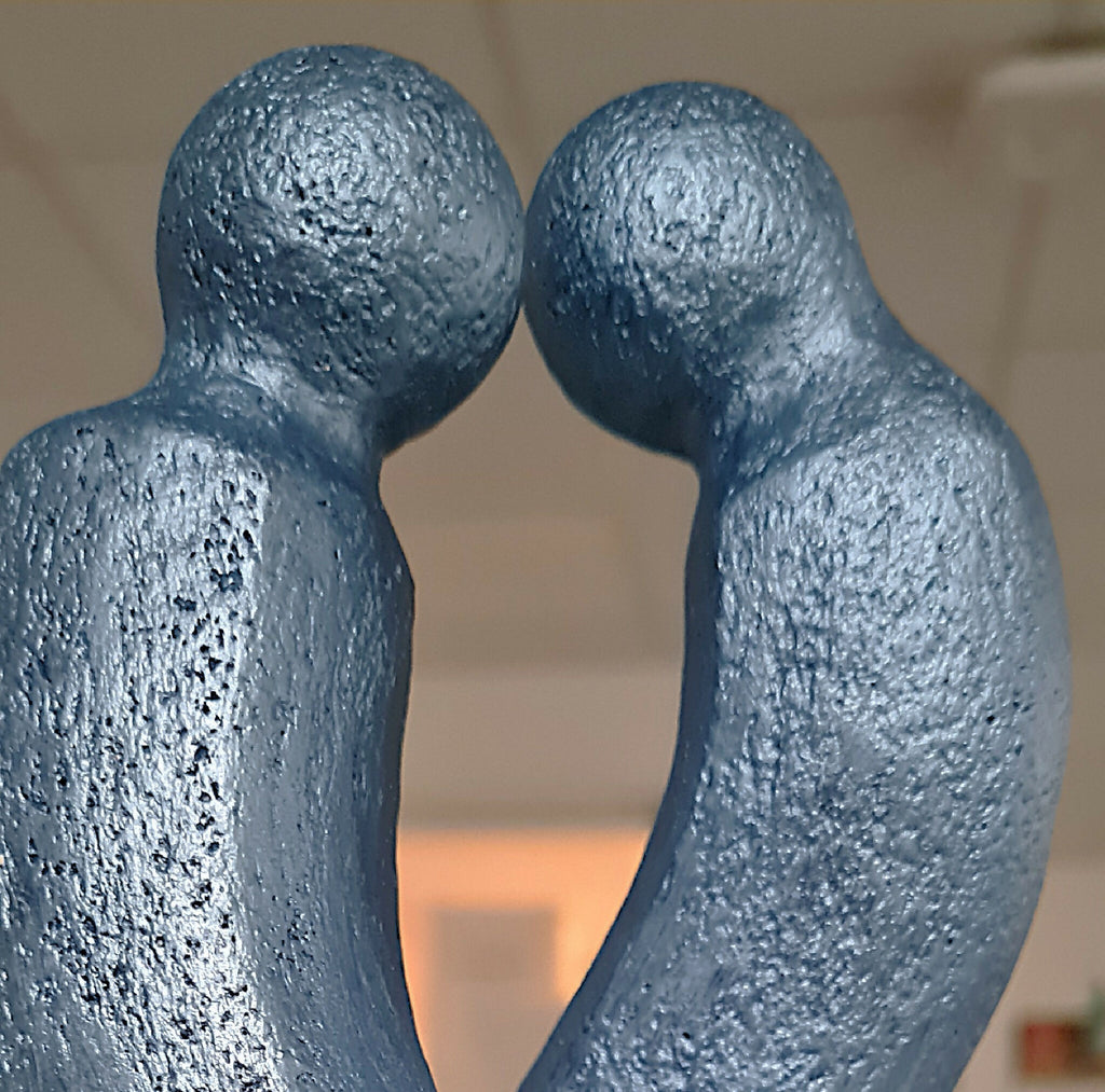 Gros plan sur sculpture couple abstrait : deux formes bleues texturées enlacées.