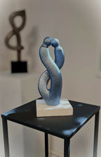 Sculpture couple abstrait en métal bleu sur socle blanc, posée sur table noire.