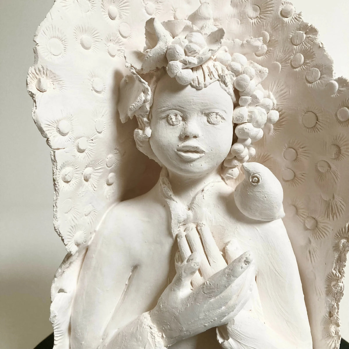 Sculpture en relief femme blanche, oiseau sur la tête, mains croisées, base noire