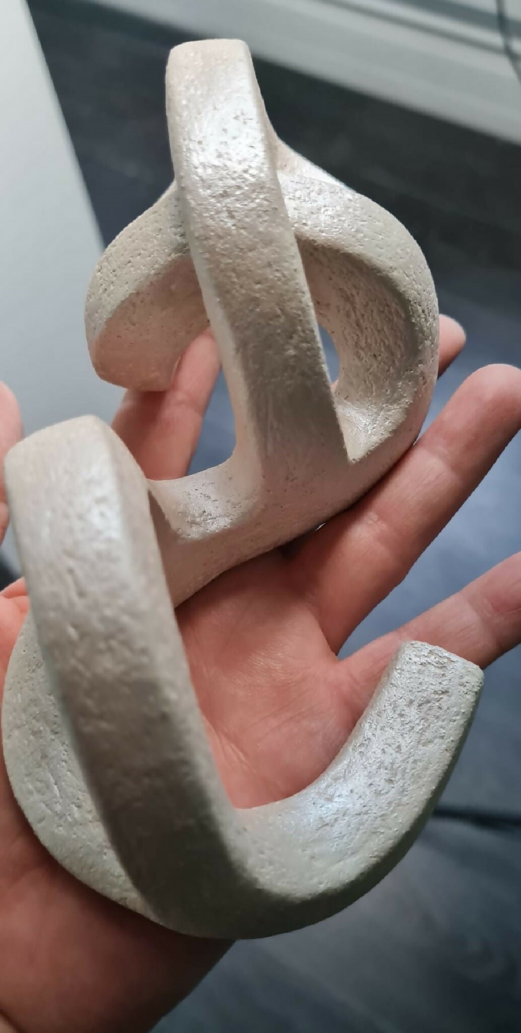 Sculpture en argile beige abstraite tenue en main, formes en anneaux ajourés