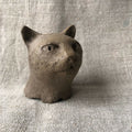 Petite sculpture en argile d’un chat, tête de face, yeux sculptés.