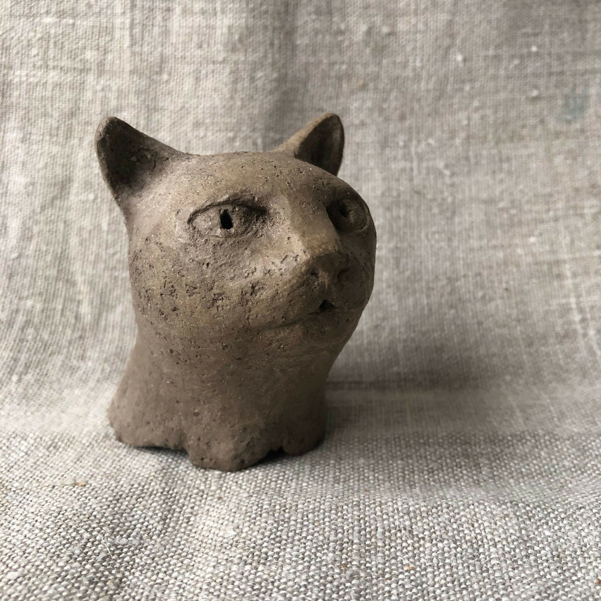 Petite sculpture en argile d’un chat, tête de face, yeux sculptés.