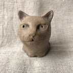 Petite sculpture en argile d’un chat, face avec museau texturé et petites ouvertures.