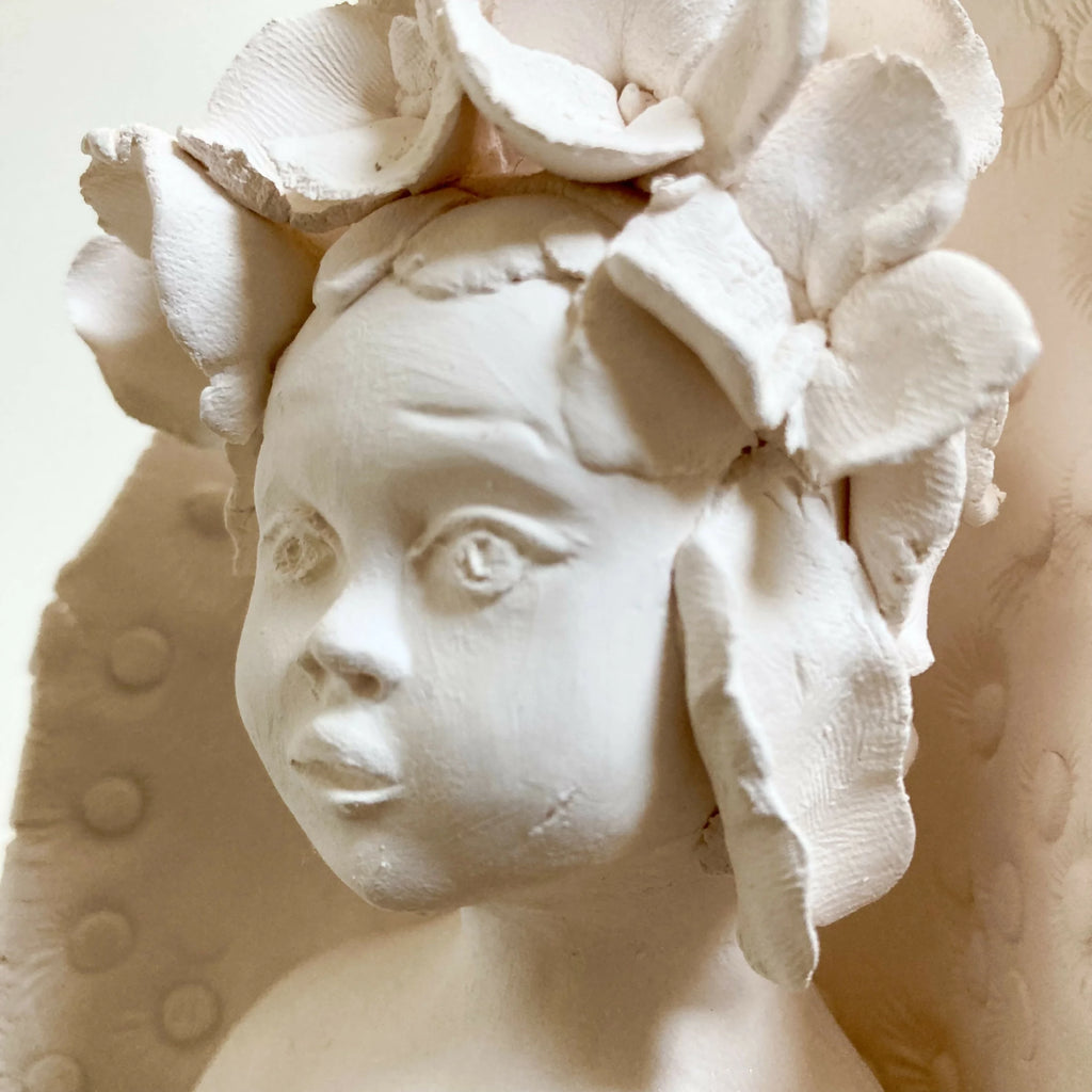 Visage d'enfant sculpté blanc, fleurs en relief autour de la tête.