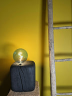 Sculpture lumineuse : ampoule sphérique vert émeraude sur base cubique bleu foncé.