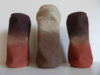 Sculptures cylindriques en trio : deux foncées et une claire, textures granuleuses.