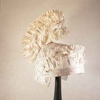 Casque à aigrette en papier froissé beige, monté sur base noire, vue de trois-quarts.