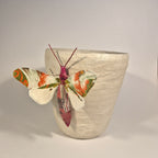 Sculpture de papillon multicolore sur pot en béton clair, vue de trois-quarts