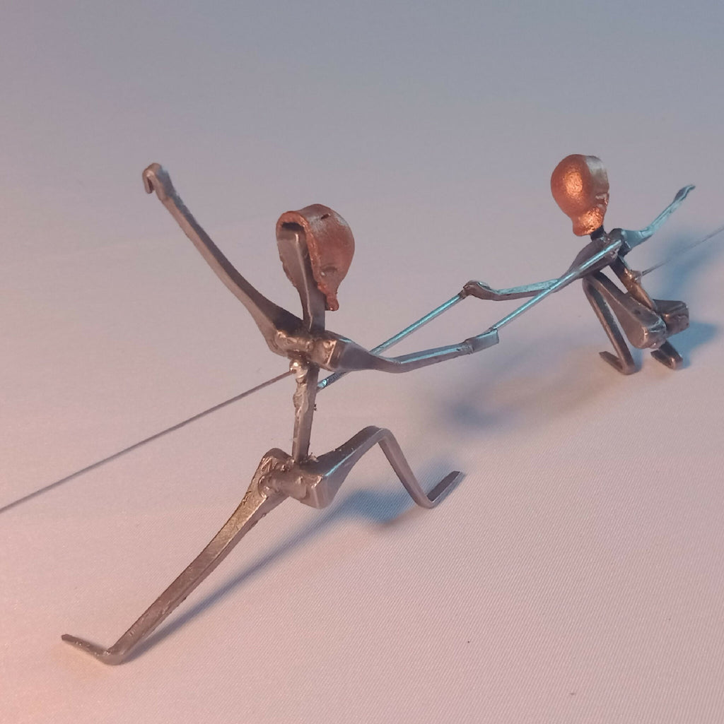 Deux escrimeuses en acier, positions en torsion, têtes cuivre, membres fins visibles.