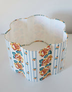 Abat-jour forme fleur en tissu bleu clair, motif floral orange, bord ondulé.