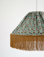 Suspension vue rapprochée : abat-jour vert à motifs floraux, franges dorées au bord.