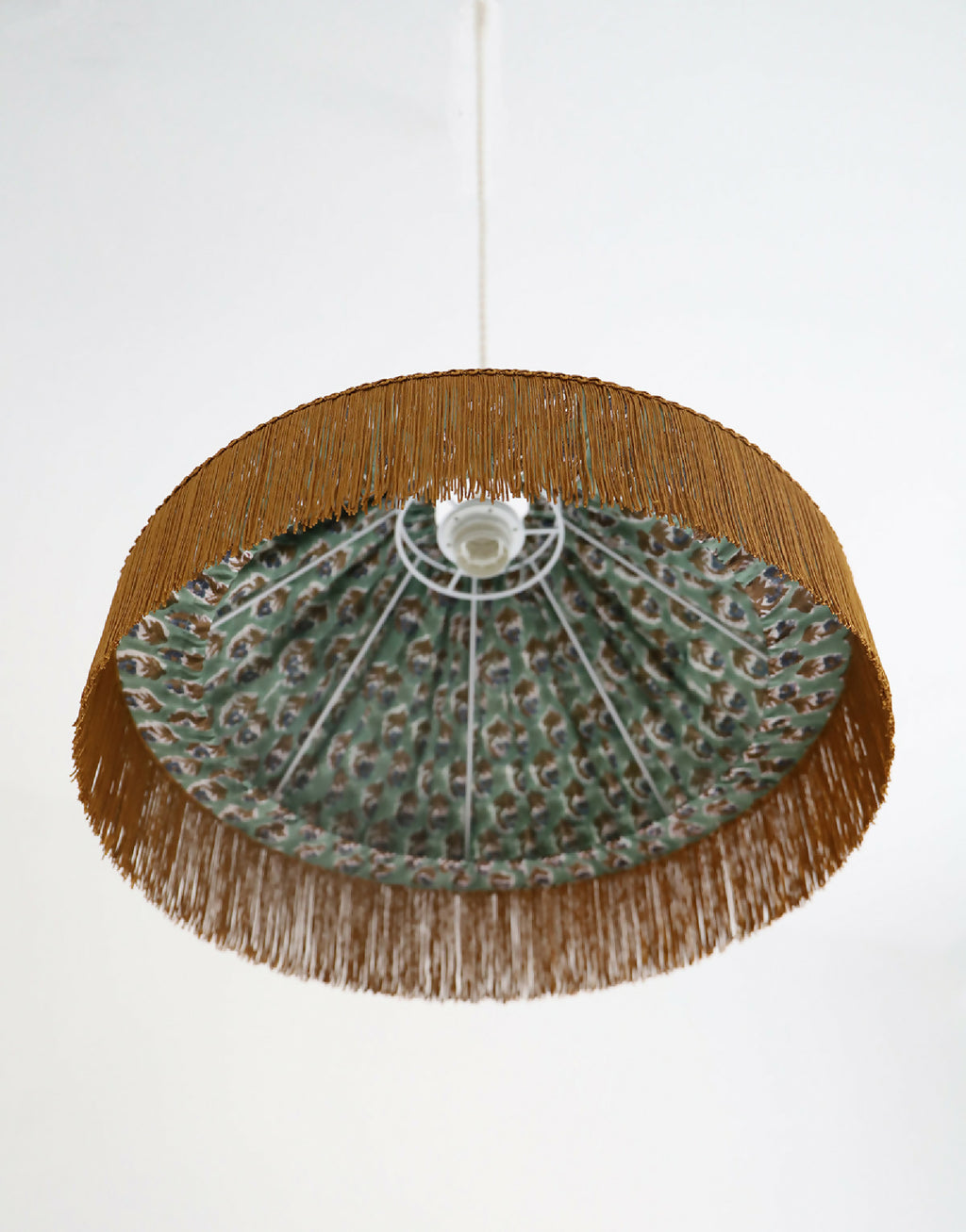 Dessous de l’abat-jour de suspension : franges dorées et intérieur de tissu à motifs.