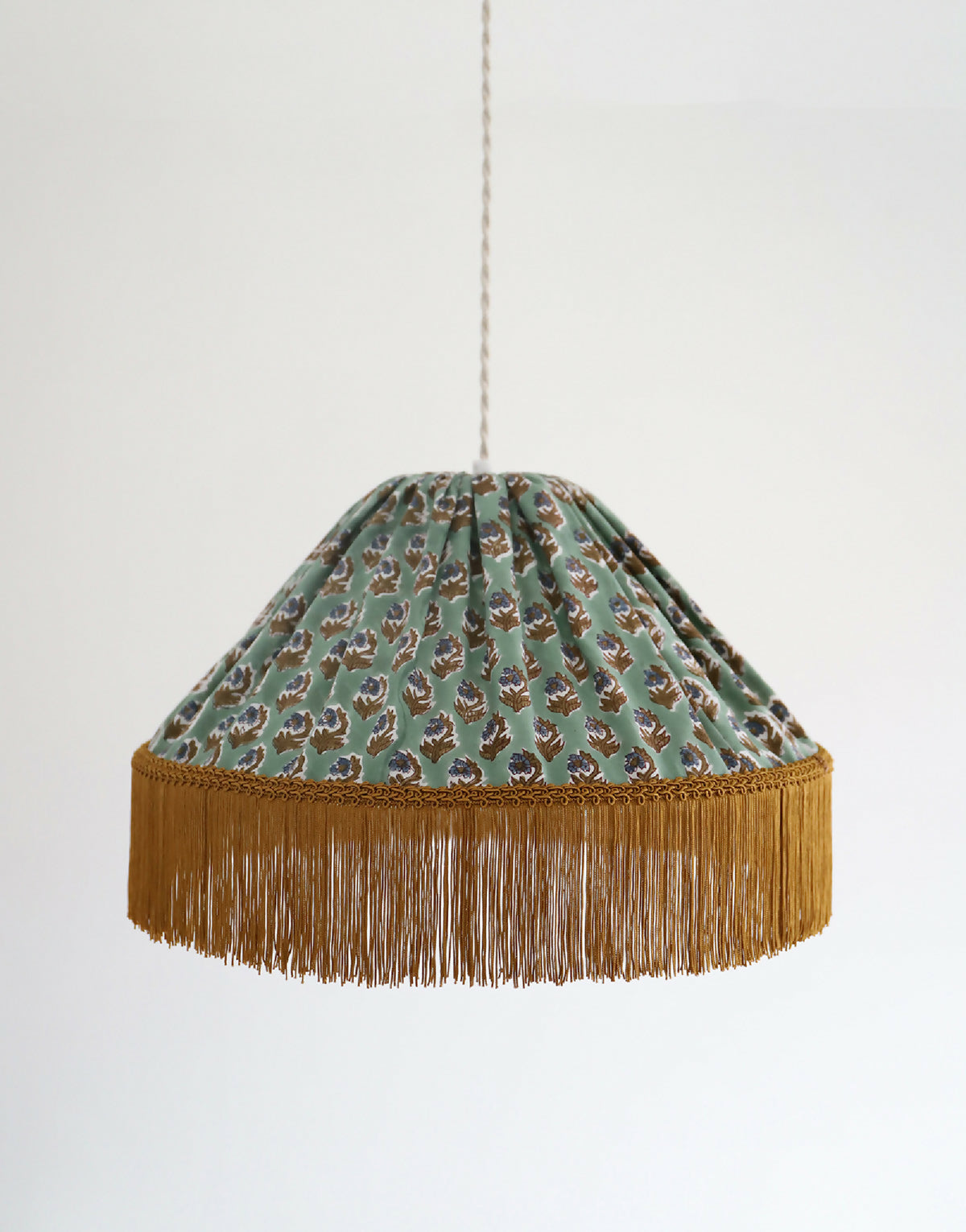 Suspension ronde à abat-jour tissu vert, motif floral discret, franges dorées en partie basse.