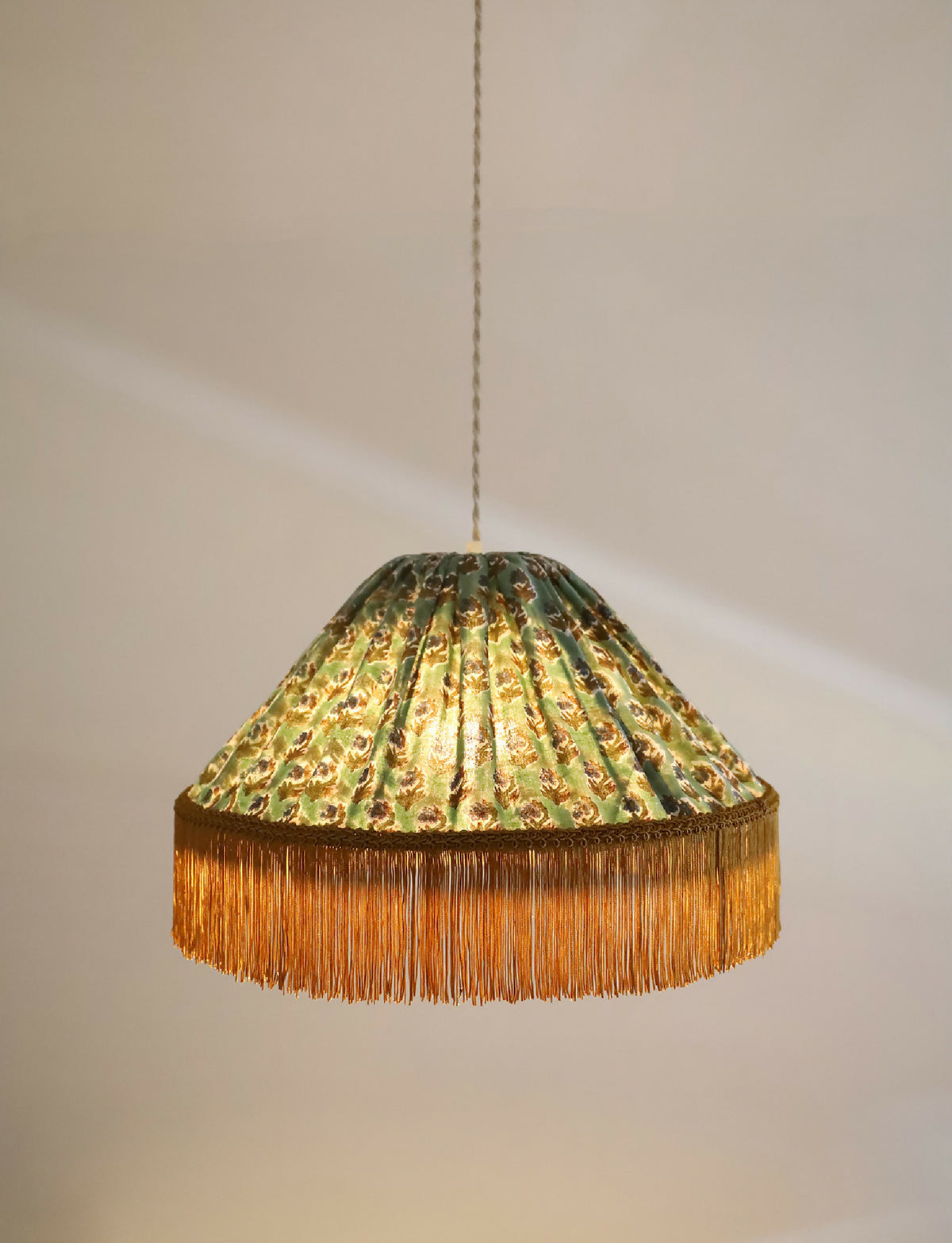 Suspension à abat-jour doré-vert à motifs, bordure dorée à franges et pendentif.