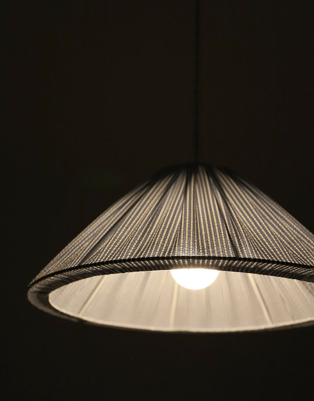 Suspension conique à fines rayures dorées, lumière allumée sous l’abat-jour.