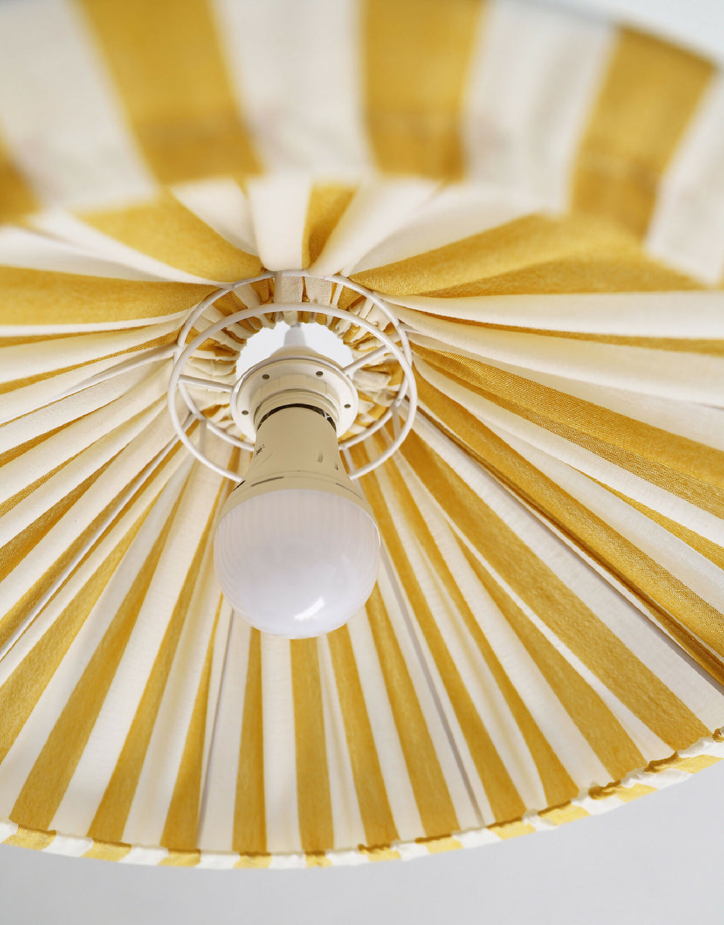Plafonnier suspendu conique rayé jaune et blanc, vue du dessous avec ampoule