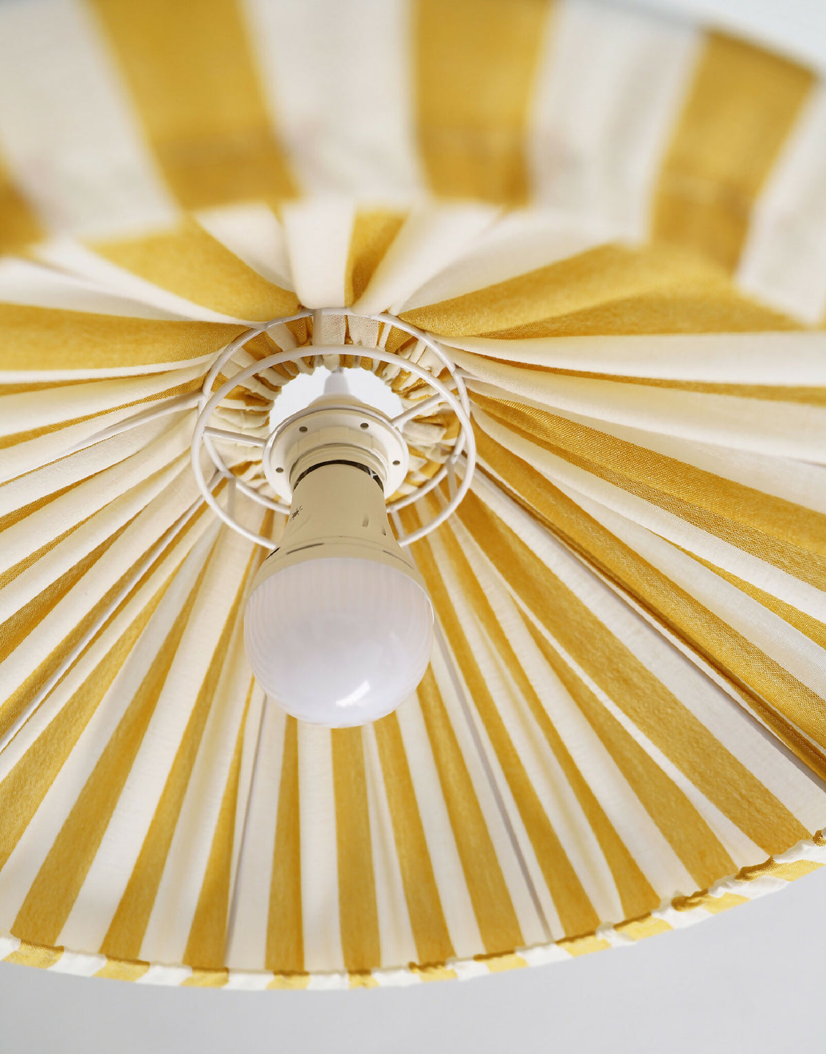 Plafonnier suspendu conique rayé jaune et blanc, vue du dessous avec ampoule