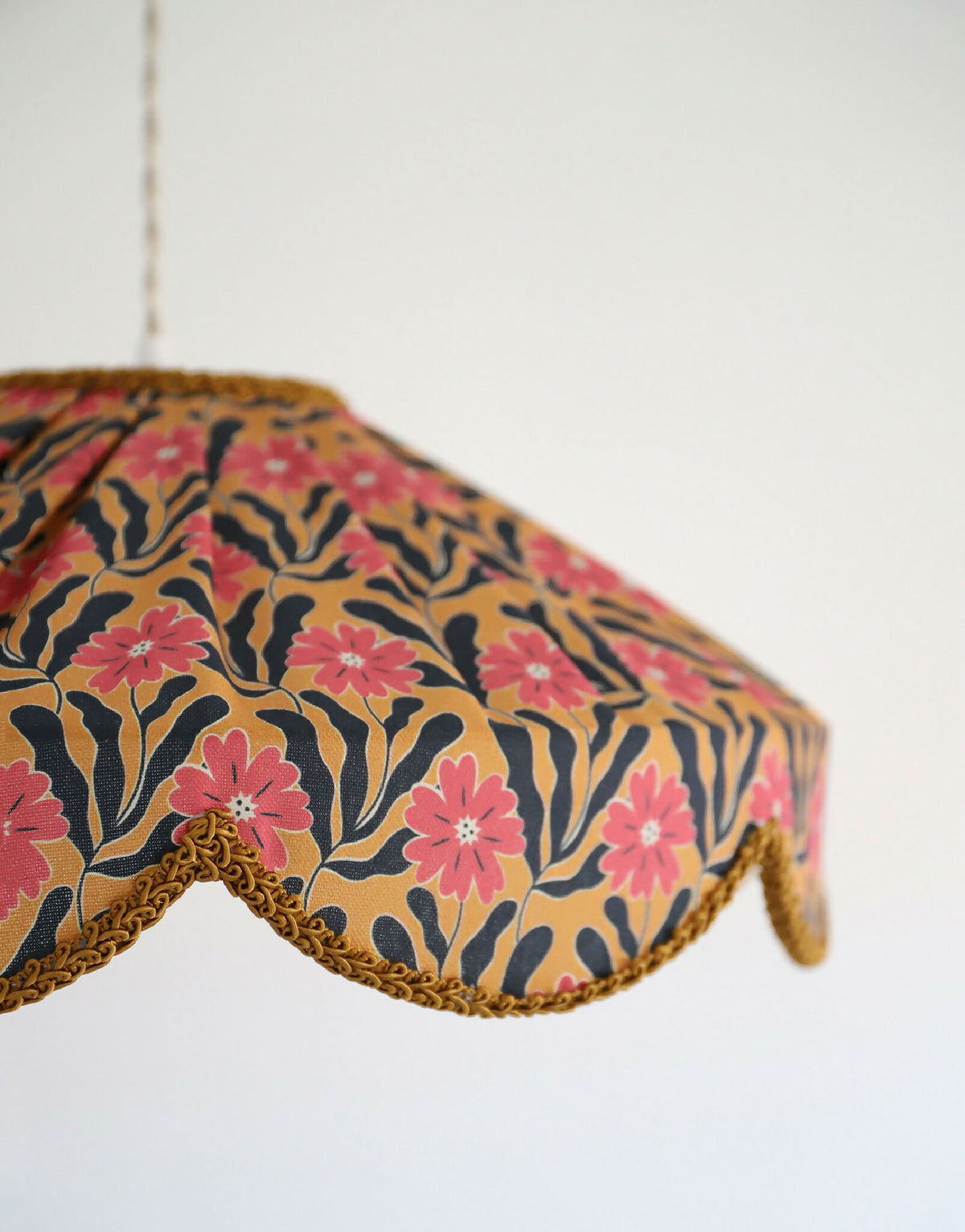 Détail de l’abat-jour festonné : tissu floral roses, bord doré tressé, forme arrondie.