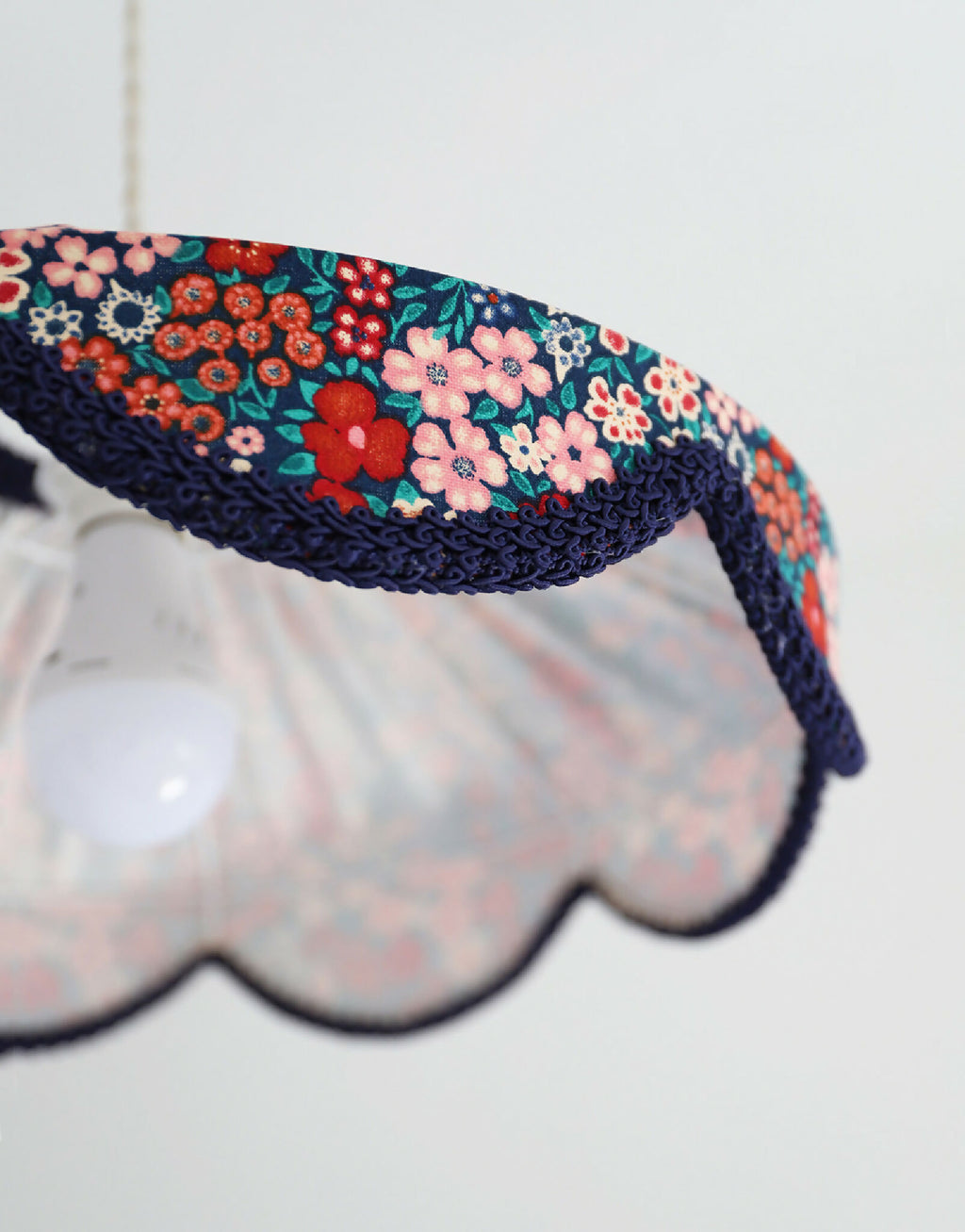Détail de l’abat-jour festonné : tissu floral mille fleurs, bord bleu marine et motif.