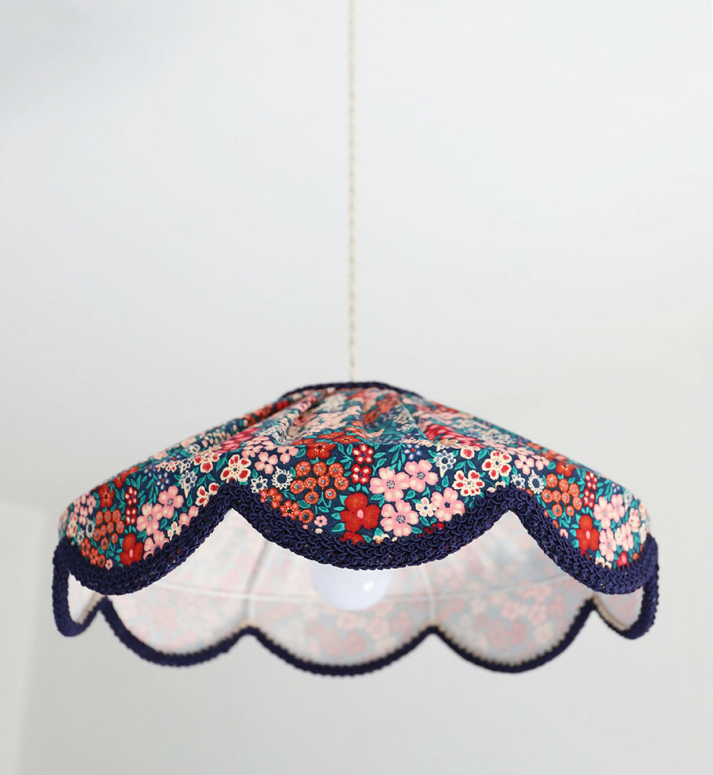 Abat-jour suspendu festonné en tissu floral mille fleurs, base blanche et bord bleu marine.