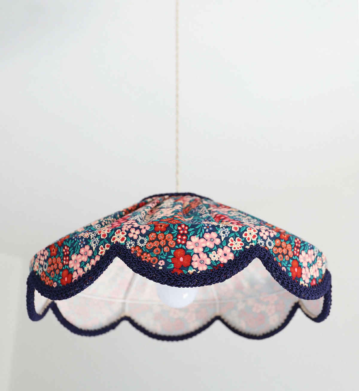 Abat-jour suspendu festonné en tissu floral mille fleurs, base blanche et bord bleu marine.