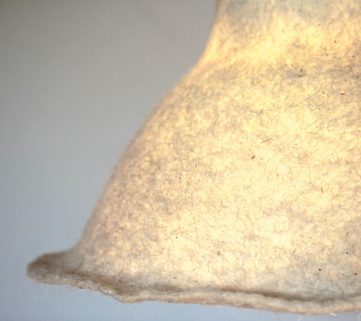 Abat-jour en feutre de laine beige clair, texture fibreuse visible, partie bois suspendue