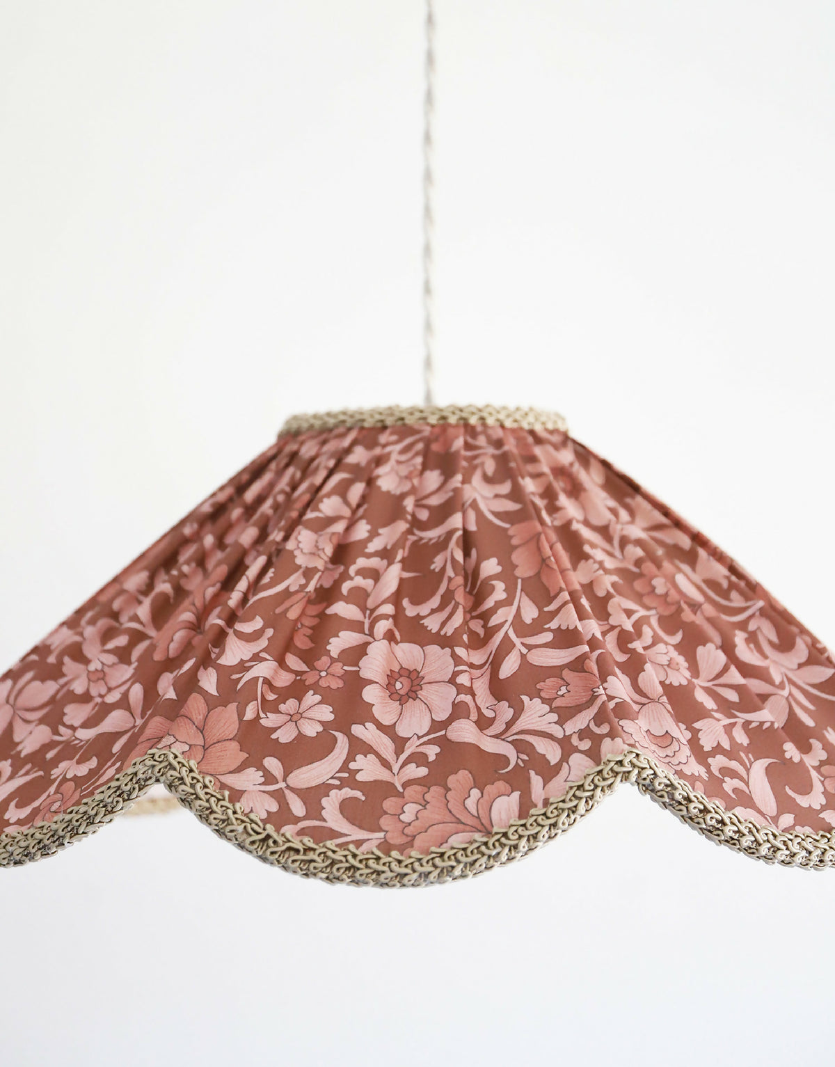 Suspension florale en tissu bordeaux, motif fleurs et bordure dorée en couronne.