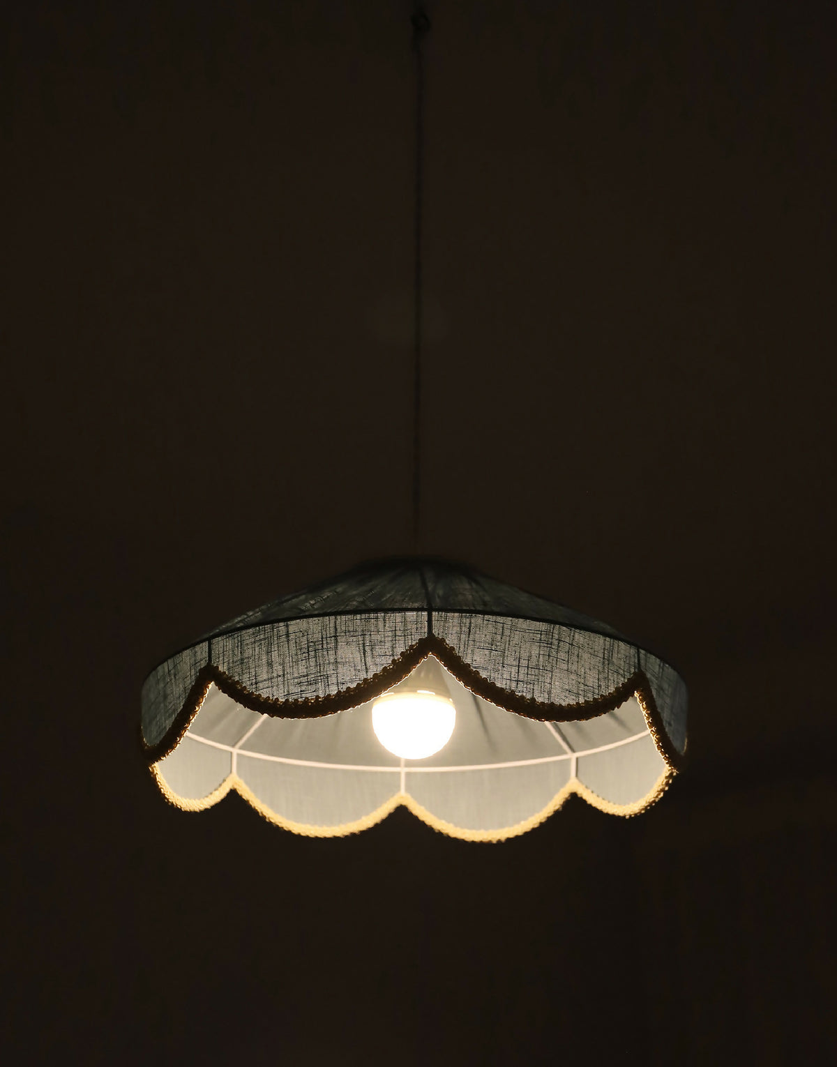 Suspension abat-jour sombre, bordure dorée festonnée, ampoule visible allumée