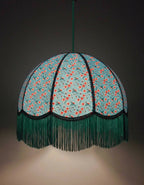 Suspension en papier bleu à motifs fleuris, franges vertes et liséré noir.