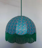 Suspension ronde en papier bleu, motifs floraux, franges vertes au bord inférieur.