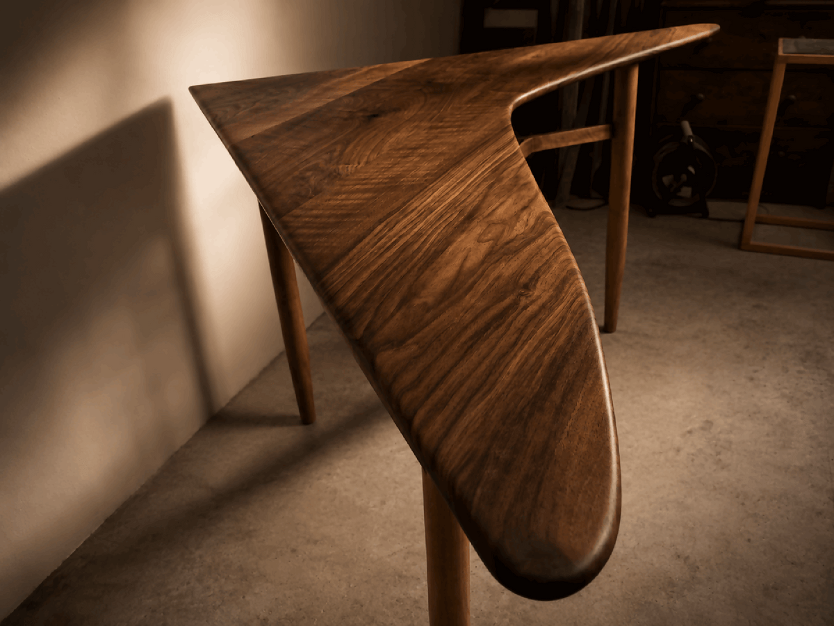 Table d’angle en bois brun, bord arrondi du piètement, pieds en bois.