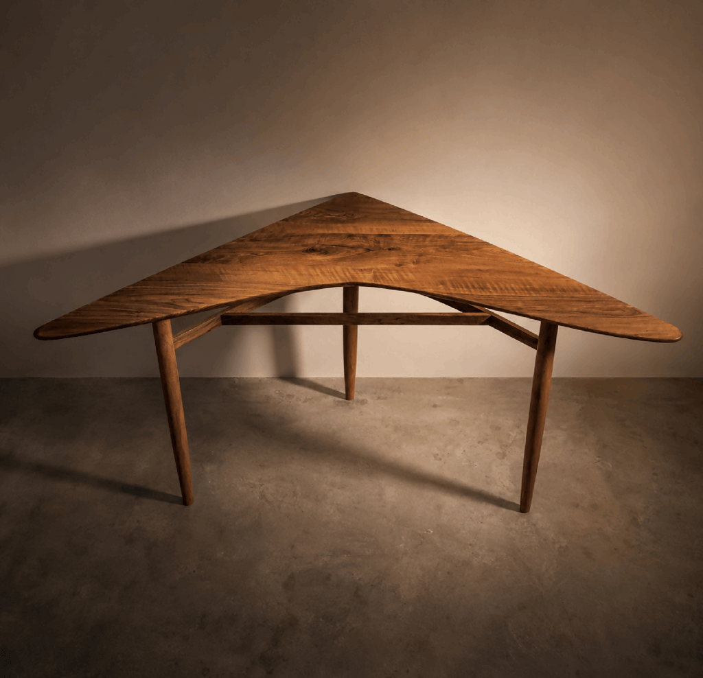 Table d’angle en bois brun, plateau cintré, structure en barreaux sous le plateau.