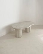 Table basse HESTIA ovale, plateau clair et pieds cylindriques cannelés visibles.